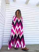 Vestido camisero largo con estampado chevron en fucsia, beige y negro, con cuello camisero, mangas largas y abotonadura frontal. Presenta aberturas laterales en el ruedo.