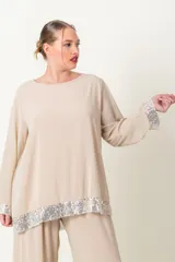 Blusa color beige con cuello redondo y mangas largas, con detalle de lentejuelas plateadas en el ruedo y los puños.