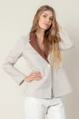 Blazer de lino color blanco con solapas y cuello en color beige, corte entallado, botón de nácar, tajo en la espalda y bolsillos laterales.