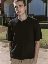 Polo negro de manga corta con cuello clásico y cierre de dos botones. Tejido de punto plano con textura ligera y fit relajado.