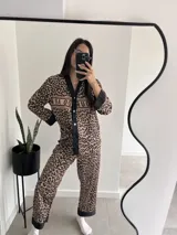 Pijama de dos piezas con estampado animal print, compuesto por camisa de manga larga con botones y pantalón largo. Presenta detalles en color negro en cuello, puños y ruedo.