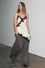 Vestido corto de satén color blanco, con tirantes finos, escote en pico y bajo asimétrico con abertura. Detalle de encaje negro en escote y ruedo.