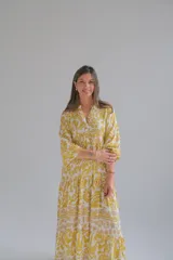 Vestido largo amarillo con estampado floral blanco, cuello en V, mangas 3/4 y corte escalonado.