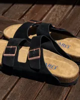 Sandalias planas de dos tiras ajustables, color negro, con hebillas metálicas color cobre. La plantilla es de corcho y látex, con forro de gamuza.