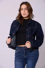 Campera de jean de color azul oscuro, con corte cropped y costuras en contraste color caramelo. Presenta cuello clásico, cierre frontal con botones metálicos y bolsillos a la altura del pecho y laterales.