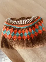 Sweater marrón tejido a mano en mohair con cuello redondo y diseño con motivos geométricos en colores blanco, rosa y celeste.
