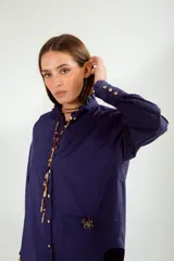 Camisa azul con cuello mao con volados, manga larga con puños con volados, cierre frontal con botones y bolsillo de parche con broche con forma de insecto.