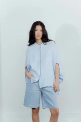 Camisa celeste de lino con corte amplio, cuello mao y mangas cortas. Presenta cierre frontal con botones y ribete negro en cuello y tapeta.