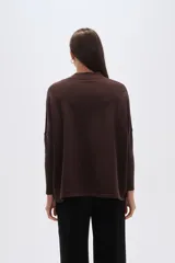 Sweater de tejido marrón oscuro con cuello alto y un gran aplique bordado en blanco con diseño abstracto que simula un abanico o flor.