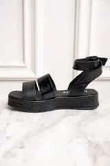 Sandalias negras de cuero con plataforma y dos tiras sobre el empeine, una de cuero liso y otra charolada. La tira del tobillo es de cuero con textura tipo cocodrilo y hebilla metálica.
