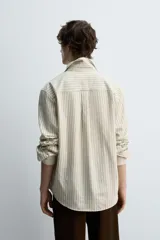 Camisa de hombre relaxed fit confeccionada en tejido de algodón a rayas verticales color beige y marrón. Tiene cuello solapa, manga larga con puños abotonados, bolsillo de parche en el pecho y cierre frontal con botones.