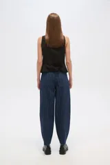 Pantalón jean negro con finas rayas verticales blancas, de corte amplio y tiro alto.