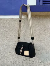 Cartera bandolera negra de nylon con detalles en charol, grifa de goma y cordones combinados. Tiene correa regulable e intercambiable.