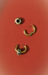 Aros tipo argolla de metal dorado con un dije colgante en forma de cuenta ovalada con estampado dálmata (blanco y negro).