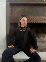 Camisa negra con cuello alto de encaje, mangas largas y cierre frontal con botones.