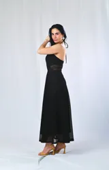 Vestido largo negro con escote halter, espalda descubierta, corte a la cintura con transparencias laterales y falda amplia con bordado calado en el ruedo.