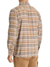 Camisa de franela a cuadros azul, beige y negro, de manga larga con puños abotonados, cuello camisero y cierre frontal con botones de madera. Tiene dos bolsillos de parche con botón en el pecho. Confeccionada en algodón orgánico cepillado.