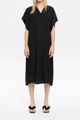 Vestido midi negro de corte recto, con escote en V pronunciado en delantero y espalda, manga corta recta con bajo descosido, cierre frontal con botonadura y fruncidos laterales en el bajo.