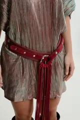 Cinturón de cuero color bordó con hebilla circular plateada y flecos largos.