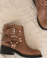 Bota corta de cuero vacuno color marrón claro, con hebillas metálicas y suela de goma negra.