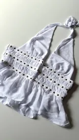 Top blanco con escote halter y espalda descubierta, confeccionado en microtul con detalle de tachas en la cintura.