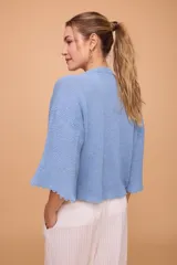 Saco tejido a máquina en lino y algodón color celeste, con silueta en línea A, mangas anchas, escote redondo con bordado en la delantera y botones de nácar. Largo por arriba de la cola.