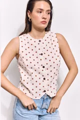 Top chaleco color arena con estampado de lunares marrones, confeccionado en tusor de algodón. Tiene corte entallado, sin mangas y cierre frontal con botones al tono.