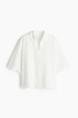 Camisa blanca de algodón con broderie, corte holgado, cuello abierto, mangas anchas al codo y ribete festoneado en mangas y bajo.