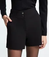 Bermuda blanca de poliéster con cintura elástica, cierre con cremallera y botones, y bolsillos laterales.