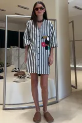 Túnica corta a rayas verticales blancas y negras con bordado de un tucán y flores rojas. Confeccionada en lino, con cuello en V y mangas 3/4. Cierre frontal con botones.