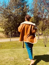 Campera gamulan color camel de cuero italiano con interior de piel sintética blanca. Tiene cuello solapa amplio, cierre con botones y bolsillos laterales.