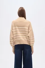 Sweater beige con rayas horizontales negras, cuello alto y corte holgado.