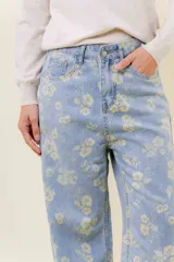 Pantalón de jean de tiro medio-alto, pierna ancha y lavado celeste claro, con estampado floral en tono amarillo pálido.