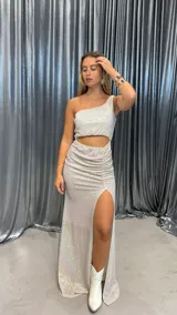 Vestido largo de fiesta con lentejuelas plateadas, corte asimétrico con un solo hombro, abertura en la cintura y tajo en la pierna.