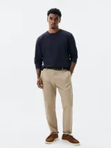 Pantalón de vestir color beige, de corte recto, con bolsillos laterales y traseros. Se ajusta a la cintura con cinturón de cuero marrón.