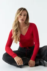 Top rojo de tejido de punto acanalado, con escote en V y mangas largas. Presenta un fruncido ajustable en el centro del frente.