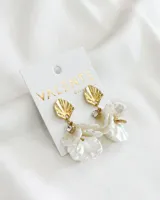 Aros colgantes con base dorada en forma de concha y detalle de strass, con pétalos de nácar blancos.