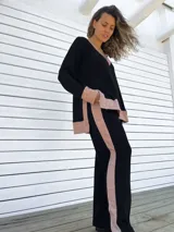Conjunto de buzo y pantalón negro con detalles en color beige. El buzo es de corte holgado, con cuello en V y puños con ribete. El pantalón es de corte recto y tiro alto.