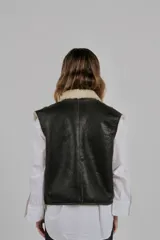 Chaleco reversible confeccionado en lambskin, con una cara de cuero en color marrón oscuro y otra de lana blanca. Presenta bolsillos frontales aplicados con ribetes de lana en contraste y diseño de cuello abierto.