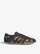 Zapatillas Adidas modelo Tokyo, color negro con bordados florales multicolores. Diseño de corte bajo con las tres tiras laterales y suela de goma color caramelo.