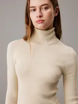 Vestido corto color crema de punto de canalé, con cuello alto y mangas largas.