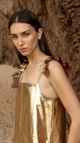 Vestido corto dorado de cuero sintético, con breteles finos regulables con volados y tajos laterales.