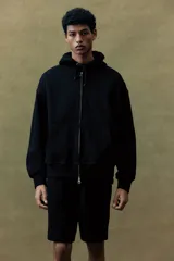 Campera con capucha negra, corte oversized, con cierre frontal, bolsillos y puños acanalados.