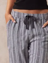 Pantalón largo de lino y rayón a rayas verticales grises y blancas. Tiene pretina elastizada con lazo de ajuste, bolsillos delanteros y traseros.
