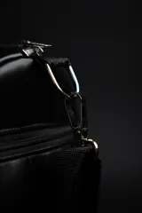 Bolso duffel negro de cuero sintético con logo de ancla bordado en rosa. Tiene doble asa de mano reforzada, correa de hombro regulable y desmontable, cierre superior con doble cremallera y tres bolsillos (dos exteriores y uno interior).