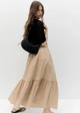 Cartera de hombro estilo hobo en color negro, confeccionada en material sintético con acabado liso. Presenta un diseño de media luna con cierre de cremallera y correa ajustable con hebilla metálica.