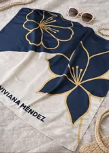 Pañuelo cuadrado de tela ligera, con diseño dividido en dos secciones: una superior azul marino y una inferior blanca. Presenta un estampado de flores grandes con contornos dorados, y el texto "VIVIANA MÉNDEZ" impreso en negro en la sección blanca.