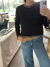 Remera negra de algodón con cuello redondo y bordados blancos en cuello, puños y ruedo. Corte recto.