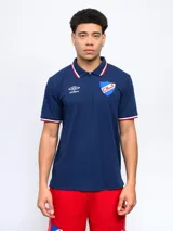 Remera polo azul con cierre, puños y cuello con detalle tricolor. Incluye logo de Umbro y escudo del Club Nacional de Football.