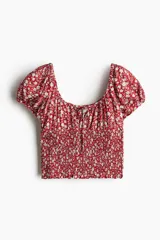 Blusa roja con estampado de flores blancas, escote cuadrado con cordón ajustable, mangas cortas abullonadas con elástico en hombros y puños, cintura fruncida y volados en mangas y bajo.